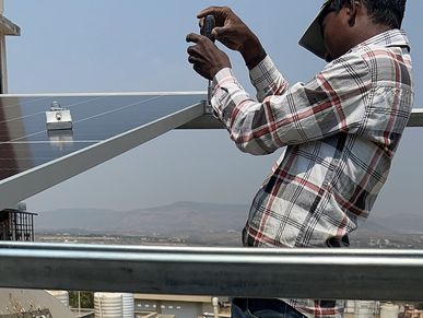 A man inspects a solar panel under a clear sky.