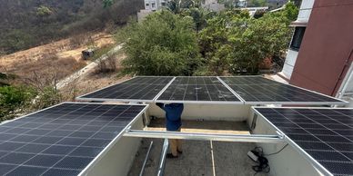 A person installs solar panels on a rooftop surrounded by trees and buildings.