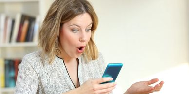 A photo of a woman looking at her smart phone with a surprised look on her face