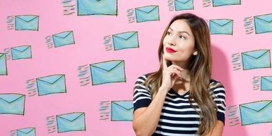 A woman looking upwards against a pink background with blue email icons