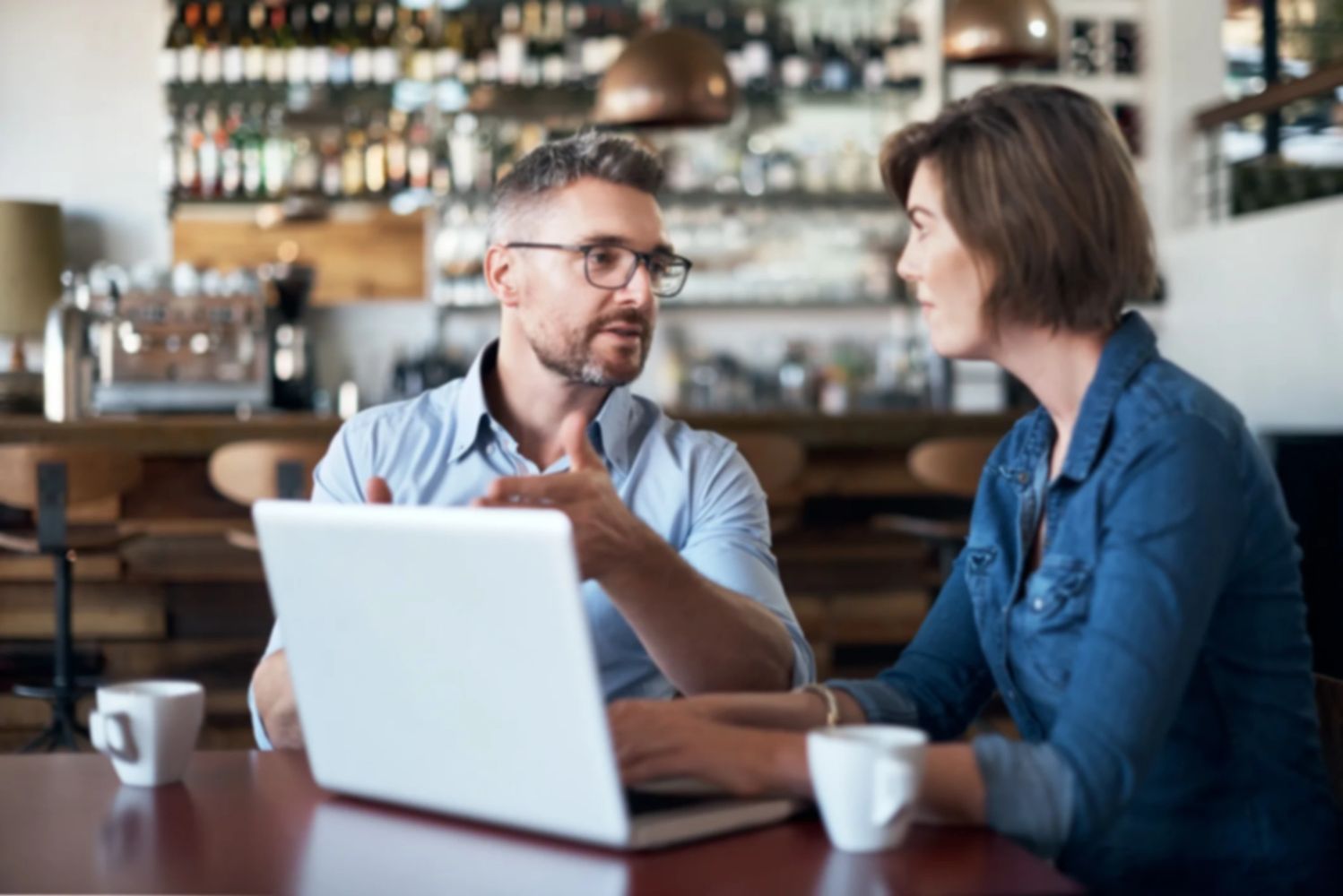 Two people engaged in a discussion over a laptop in a cozy café.