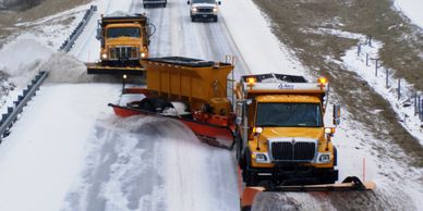 A fleet of commercial snow plowing trucks clearing a large, multi-lane road in Surrey, BC.