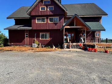 Large rustic red house with multiple windows and a gravel driveway.