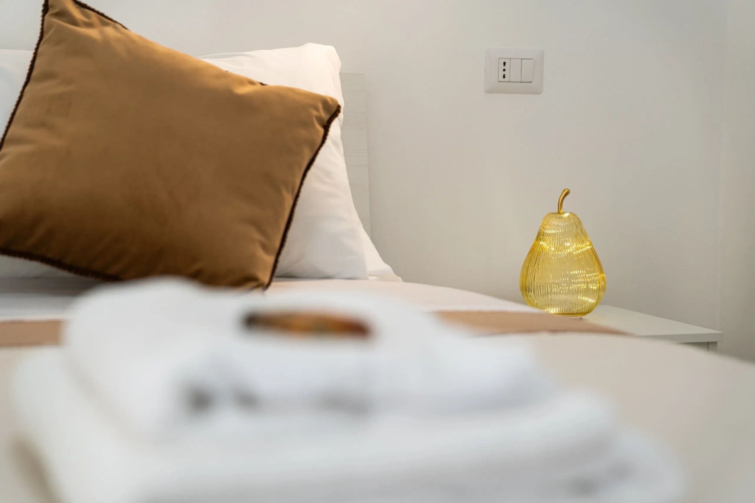 Cozy bed with brown pillow and decorative yellow glass pear on bedside table.