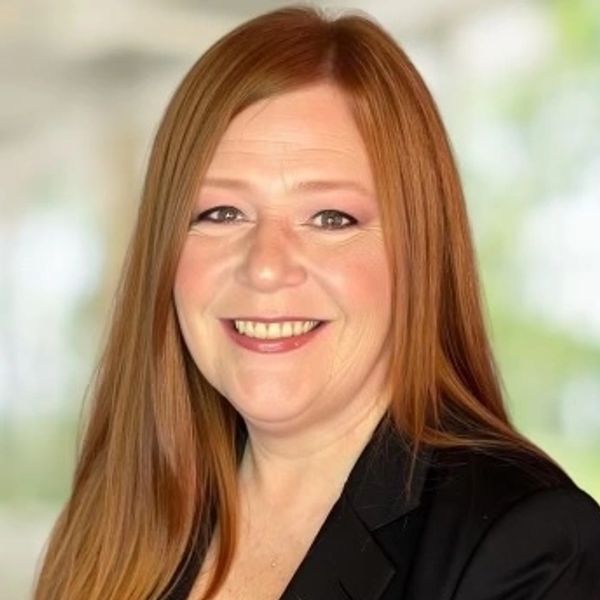 Smiling woman with long red hair in a black blazer.