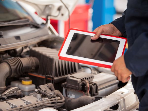A mechanic with a tablet, inspecting a car