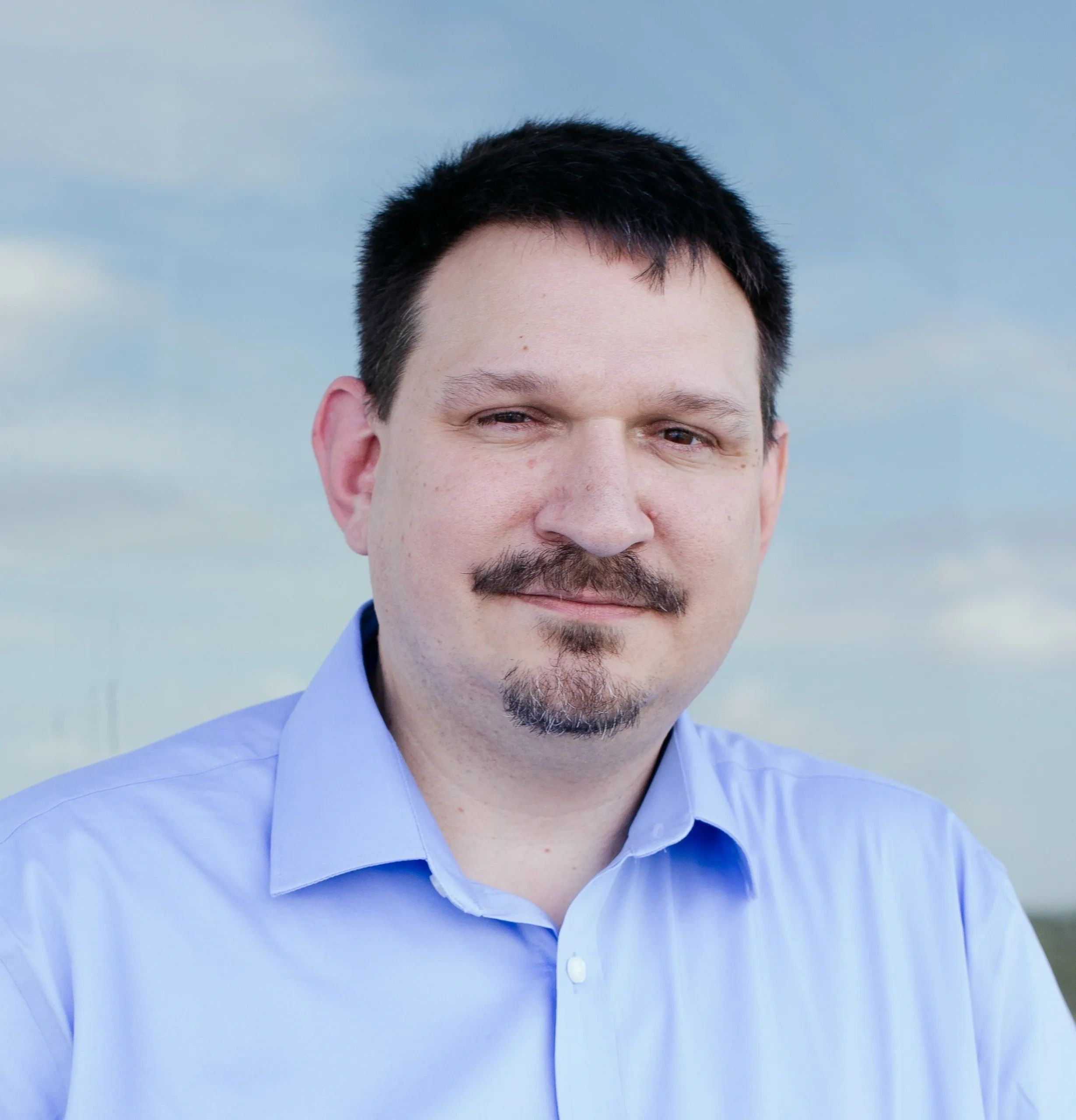 Man with mustache and goatee smiling outdoors.