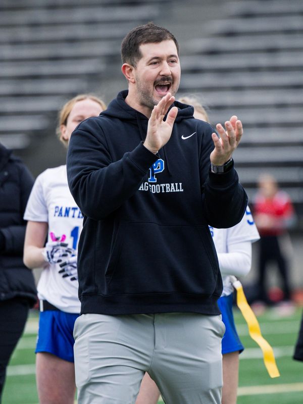 Coach clapping and encouraging players on a sports field.
