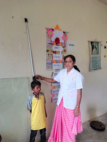 A woman in a white coat measures a boy's height in a classroom setting.