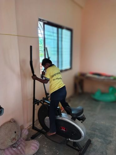 A child in a yellow shirt using an elliptical exercise machine indoors.