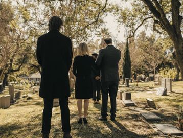 People dressed in black attending a graveside service in a cemetery.