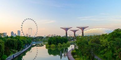 Cityscape with a ferris wheel, futuristic trees, and a river at sunset.