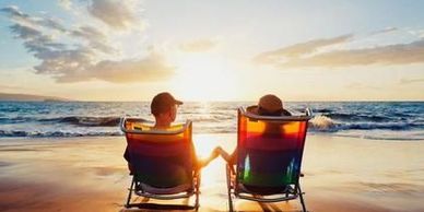Couple holding hands sitting on beach chairs watching sunset.