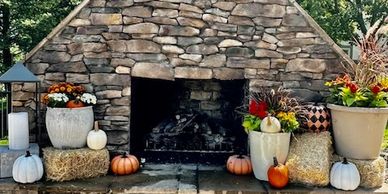 Outdoor stone fireplace decorated with pumpkins and flowers for fall.