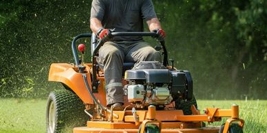Man mowing lawn with a large orange riding mower.