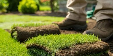 Rolled sod stacked on a freshly prepared lawn with a gardener's feet nearby.