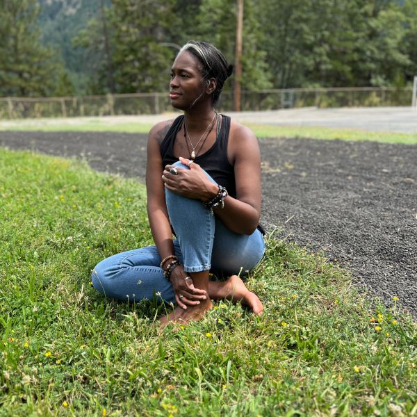 Woman sitting barefoot on grass, looking contemplative.