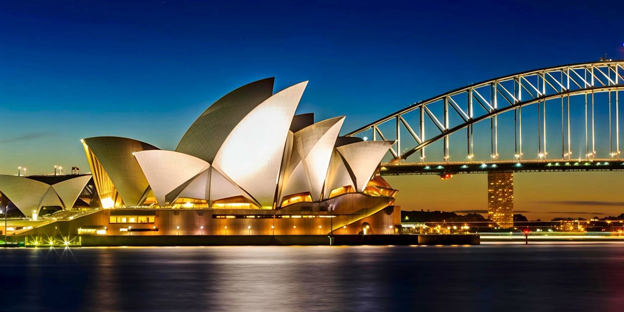 Sydney Opera House and Harbour Bridge illuminated at night.