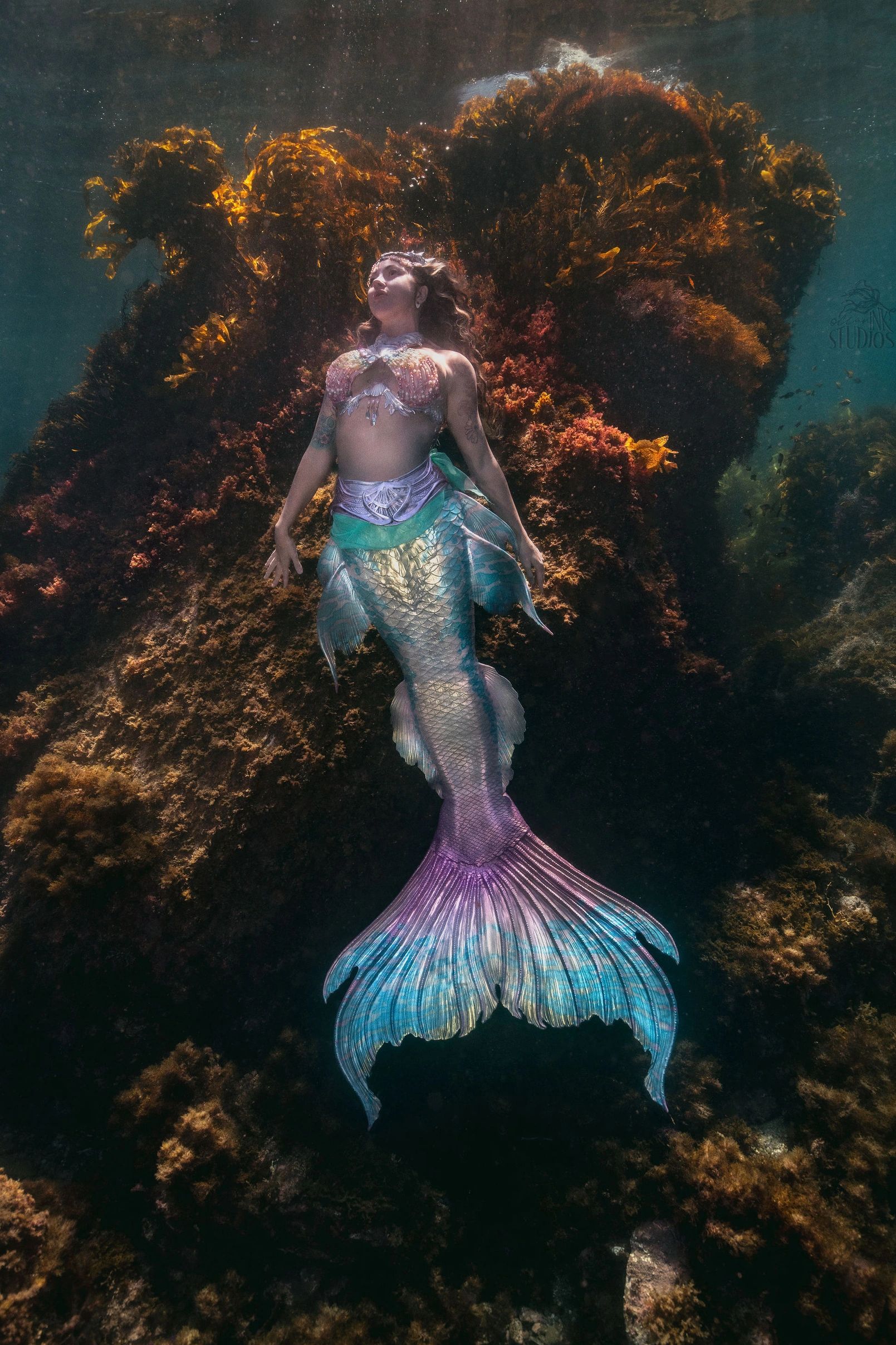 A woman dressed as a colorful mermaid underwater.