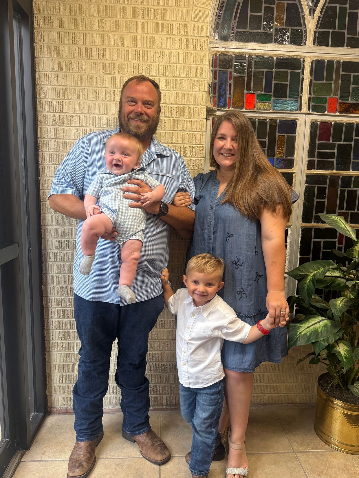 Happy family of four posing indoors by a stained glass window.