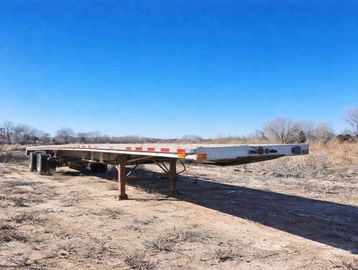 Flatbed trailer parked on a dry, dirt ground.