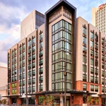 Modern multi-story building with glass windows in an urban setting under a cloudy sky.