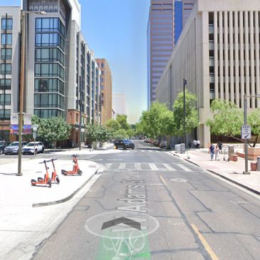 Urban street scene with scooters, tall buildings, and pedestrians on a sunny day.
