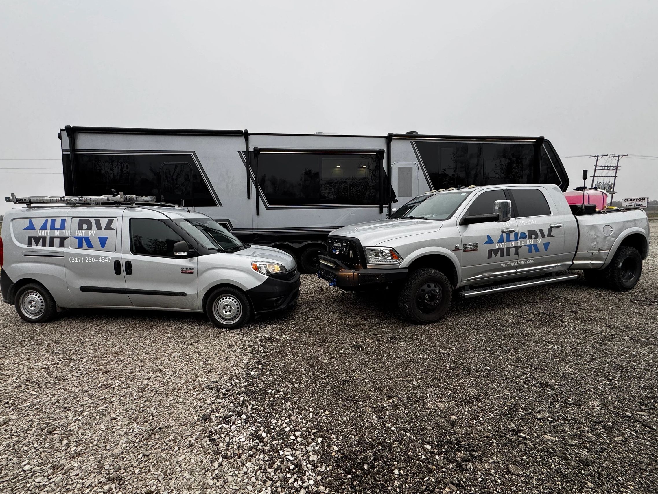 Two service vehicles and a large RV camper on gravel.