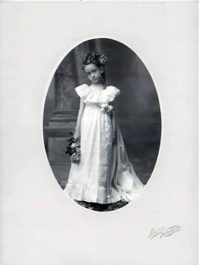 Vintage portrait of a young girl in a white dress holding flowers.