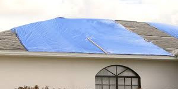 A home with a blue tarp covering the damaged section of the roof.