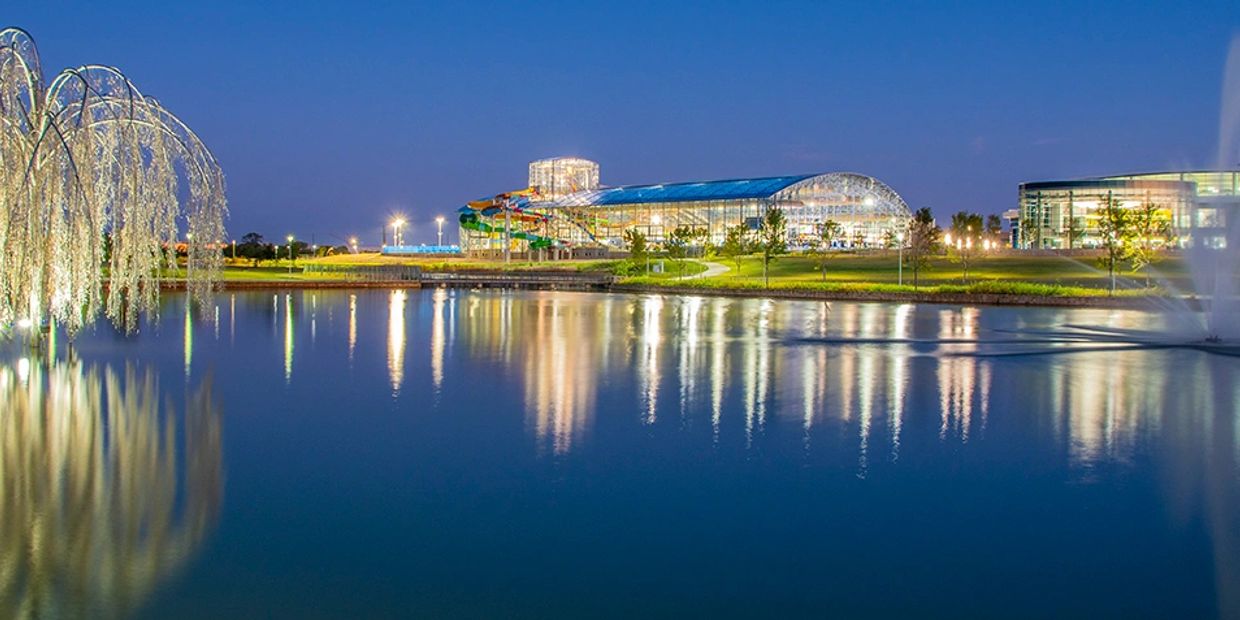 Illuminated building complex by a lake at dusk.