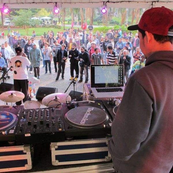Dj no primeiro plano com os toca discos e o público no fundo