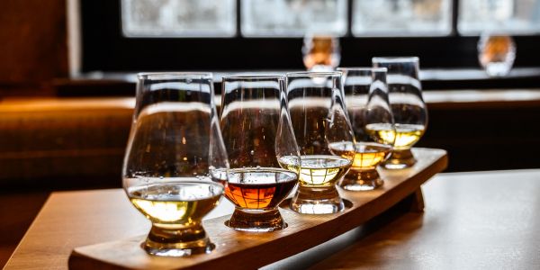A flight of whisky samples in glasses on a wooden tray.