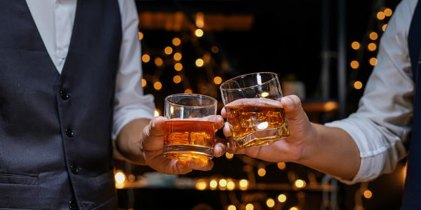 Two people toasting with whiskey glasses in a dimly lit setting.