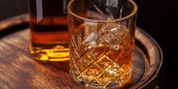 Glass of whiskey with ice on a wooden barrel.
