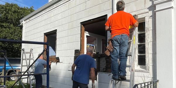 Three men working on house exterior renovation.