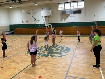 Children practicing baton twirling in a gymnasium with an instructor.
