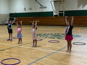 A group of young children and an instructor holding batons in a gymnasium.