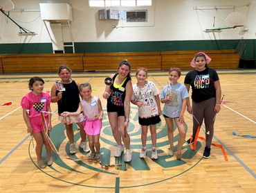 A joyful group of children and a teacher posing with colorful ribbons and props in a gym.