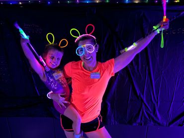 Two people wearing neon accessories and glowing under blacklight, striking a joyful pose.