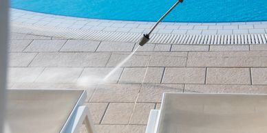 Professional pressure washing of poolside patio tiles to remove dirt and grime.