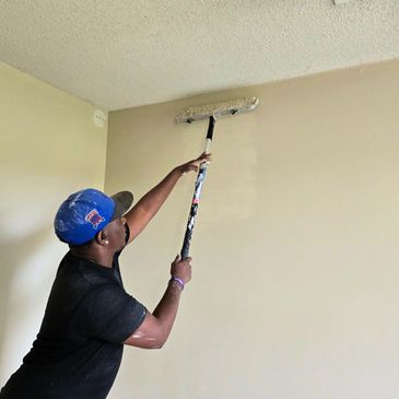 Professional painter applying fresh interior wall paint with a roller extension.