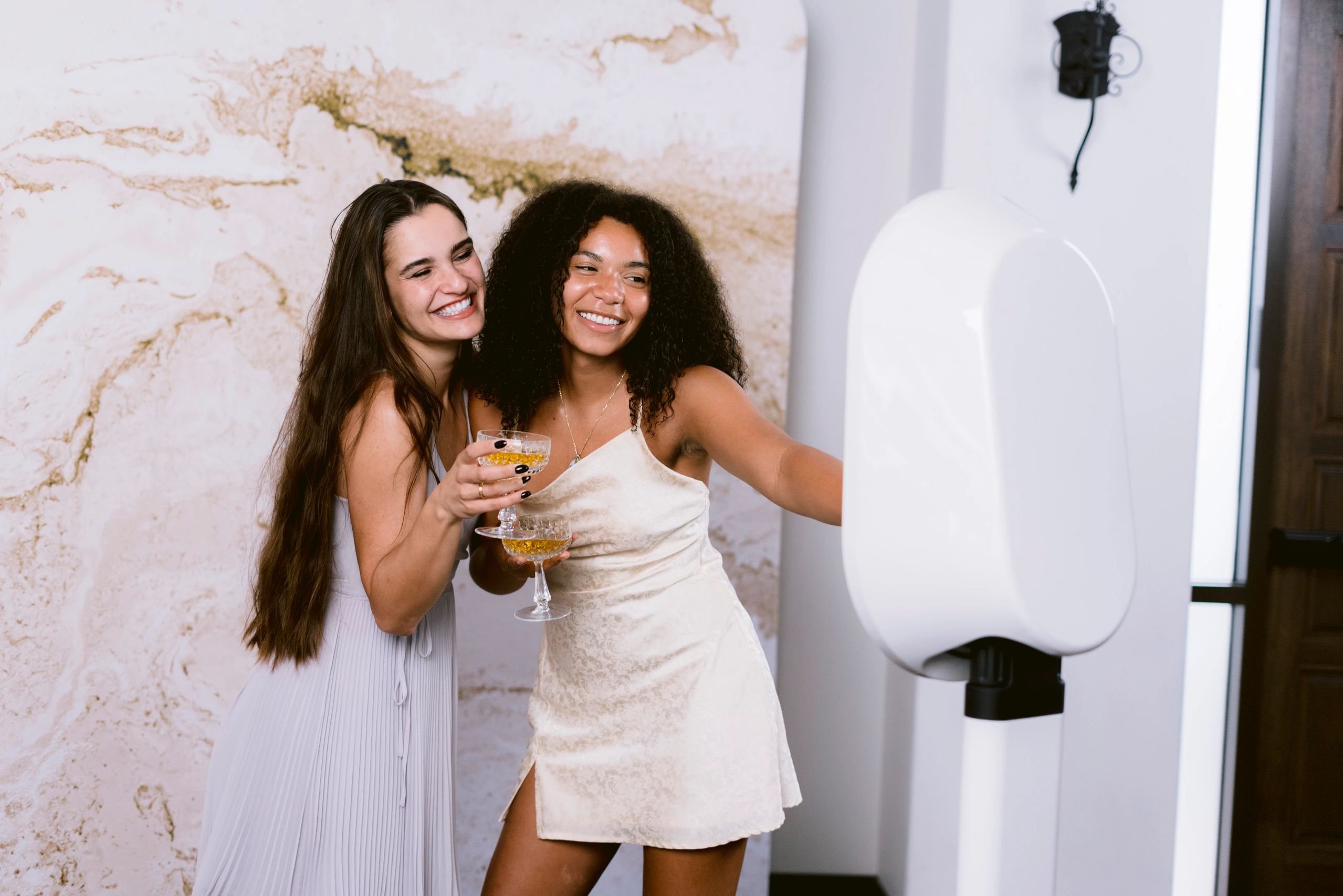 Two women smiling and posing with drinks.