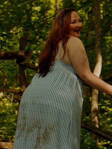 A woman in a striped dress smiles outdoors in a forest setting.