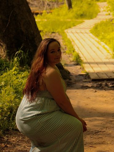 Woman in a striped dress sitting on a path in nature.