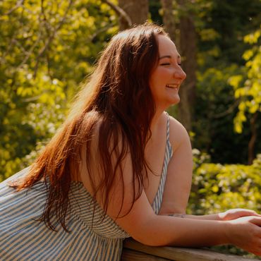 A woman with long hair smiling outdoors in sunlight.