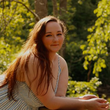 Young woman with long hair smiling outdoors in sunlight.