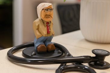 Wooden doctor figurine with glasses on a stethoscope.