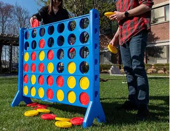 Two people playing a large outdoor Connect Four game on grass.
