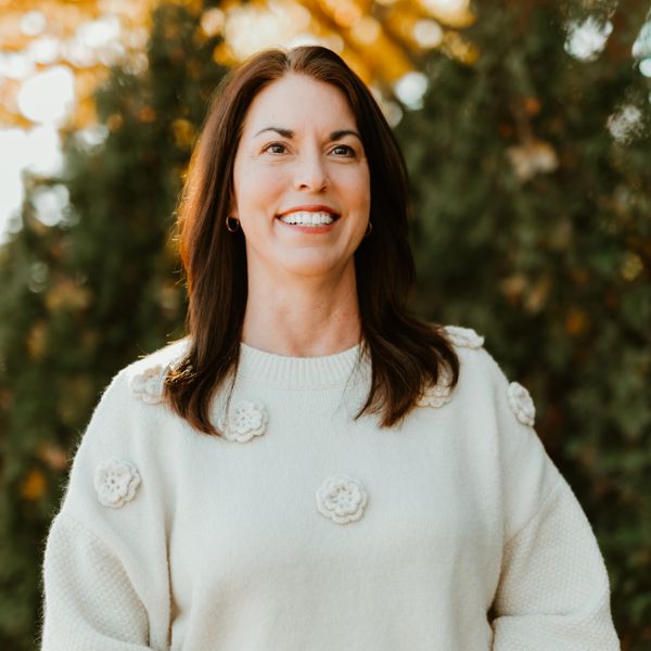 Smiling woman wearing a white sweater with flower details outdoors.